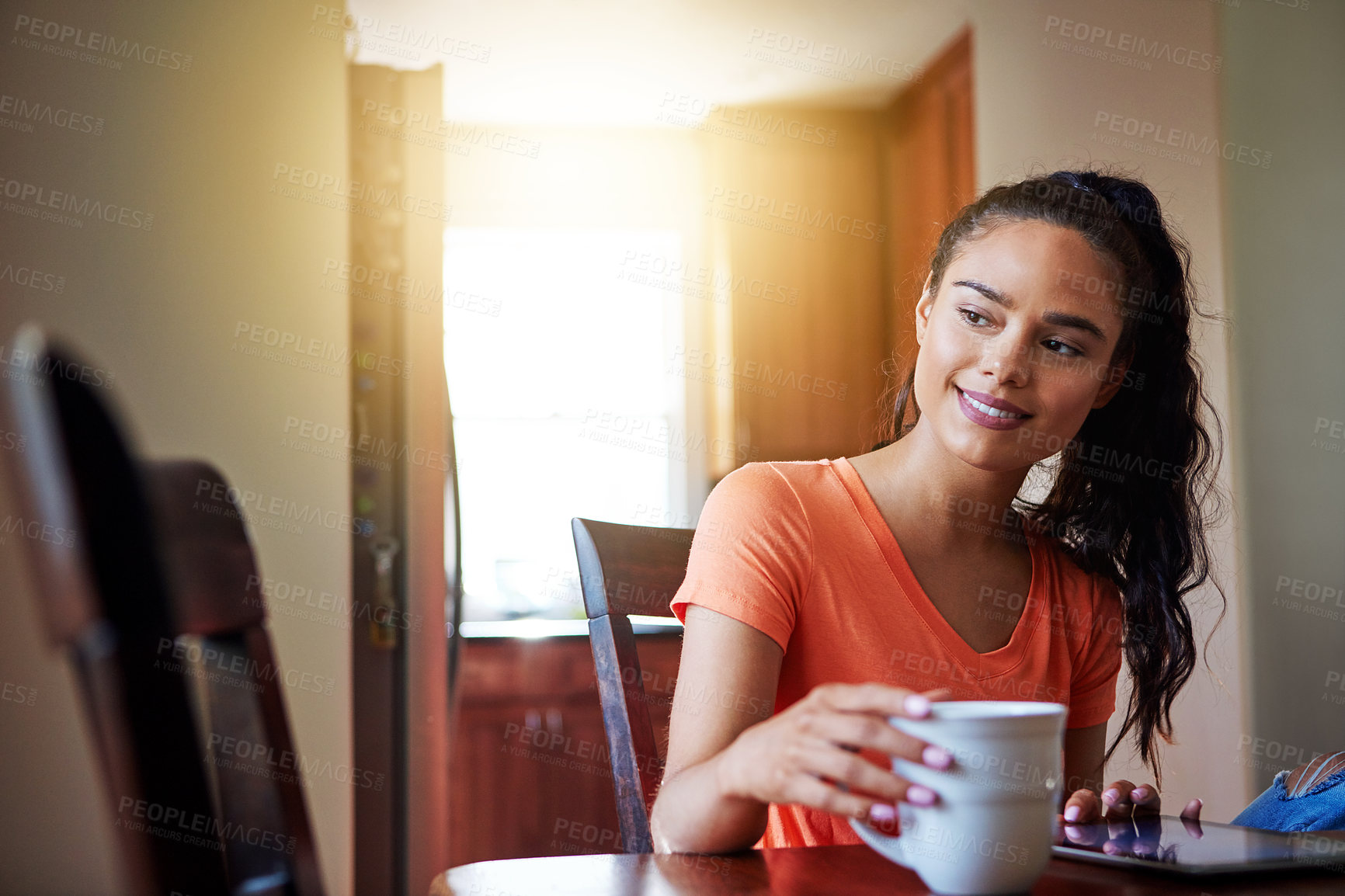 Buy stock photo Shot of a smiling young woman sitting at her dining table at home drinking coffee and using a digital tablet