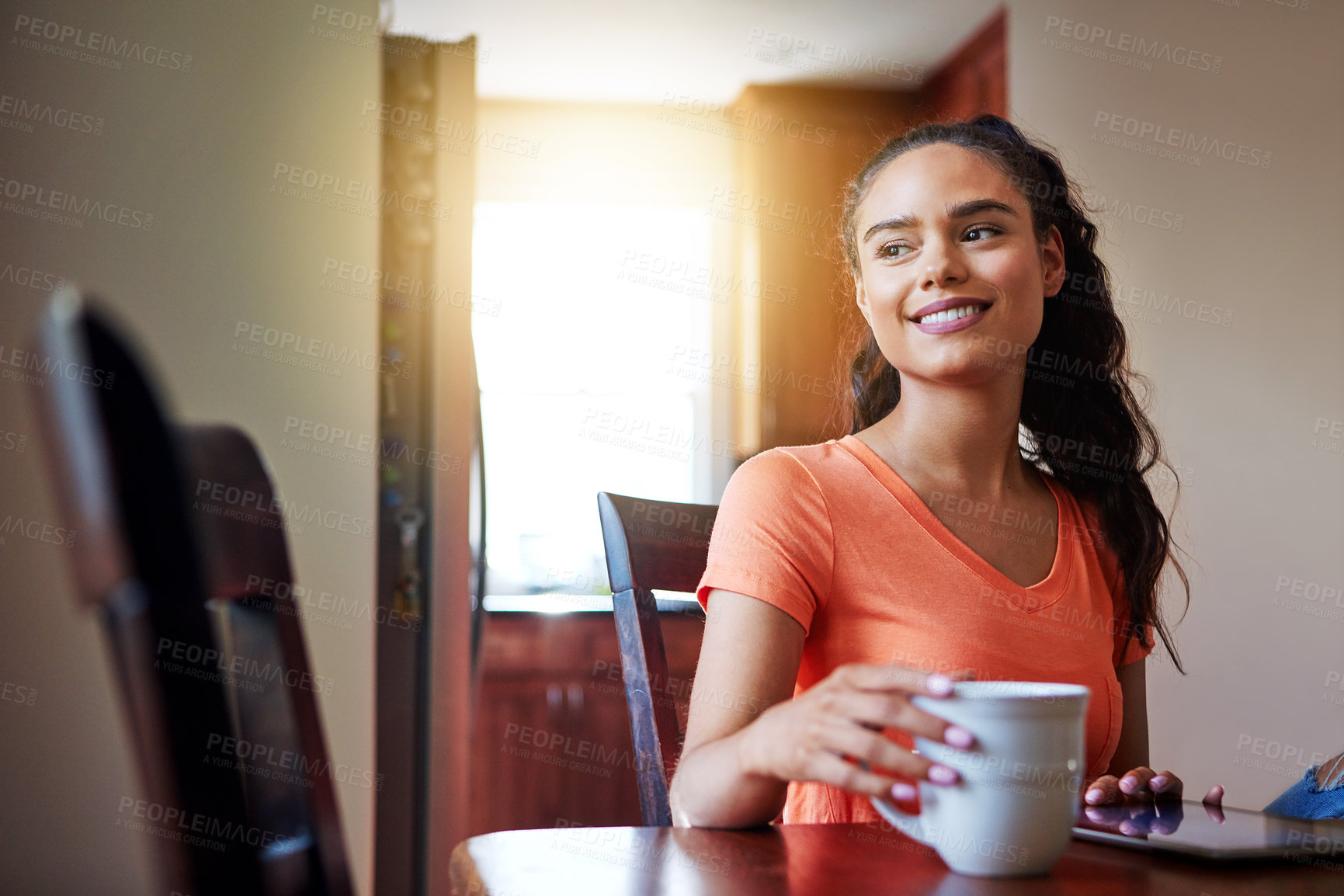 Buy stock photo Shot of a smiling young woman sitting at her dining table at home drinking coffee and using a digital tablet