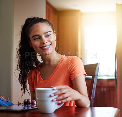Buy stock photo Shot of a smiling young woman sitting at her dining table at home drinking coffee and using a digital tablet