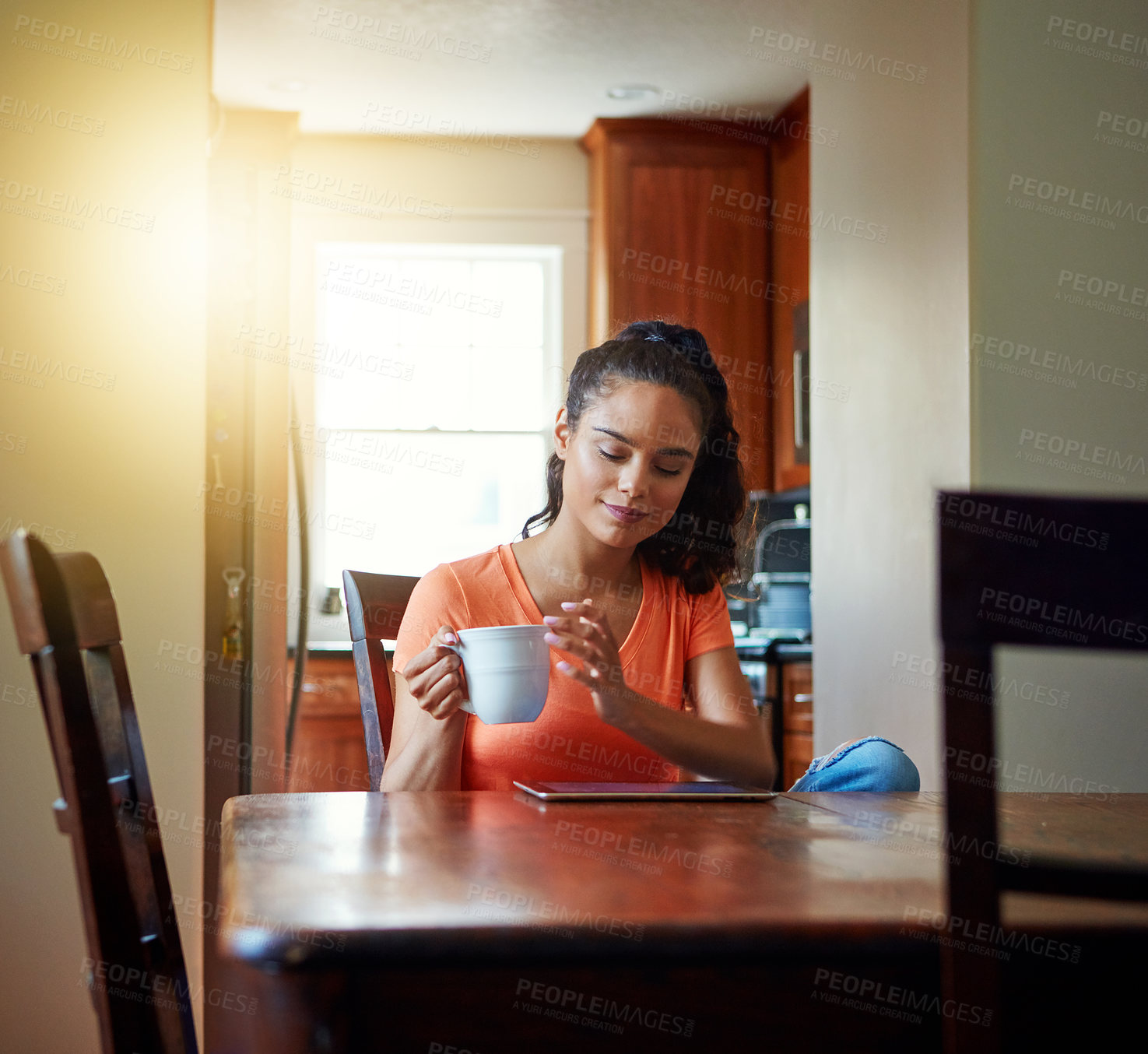 Buy stock photo Shot of a smiling young woman sitting at her dining table at home drinking coffee and using a digital tablet