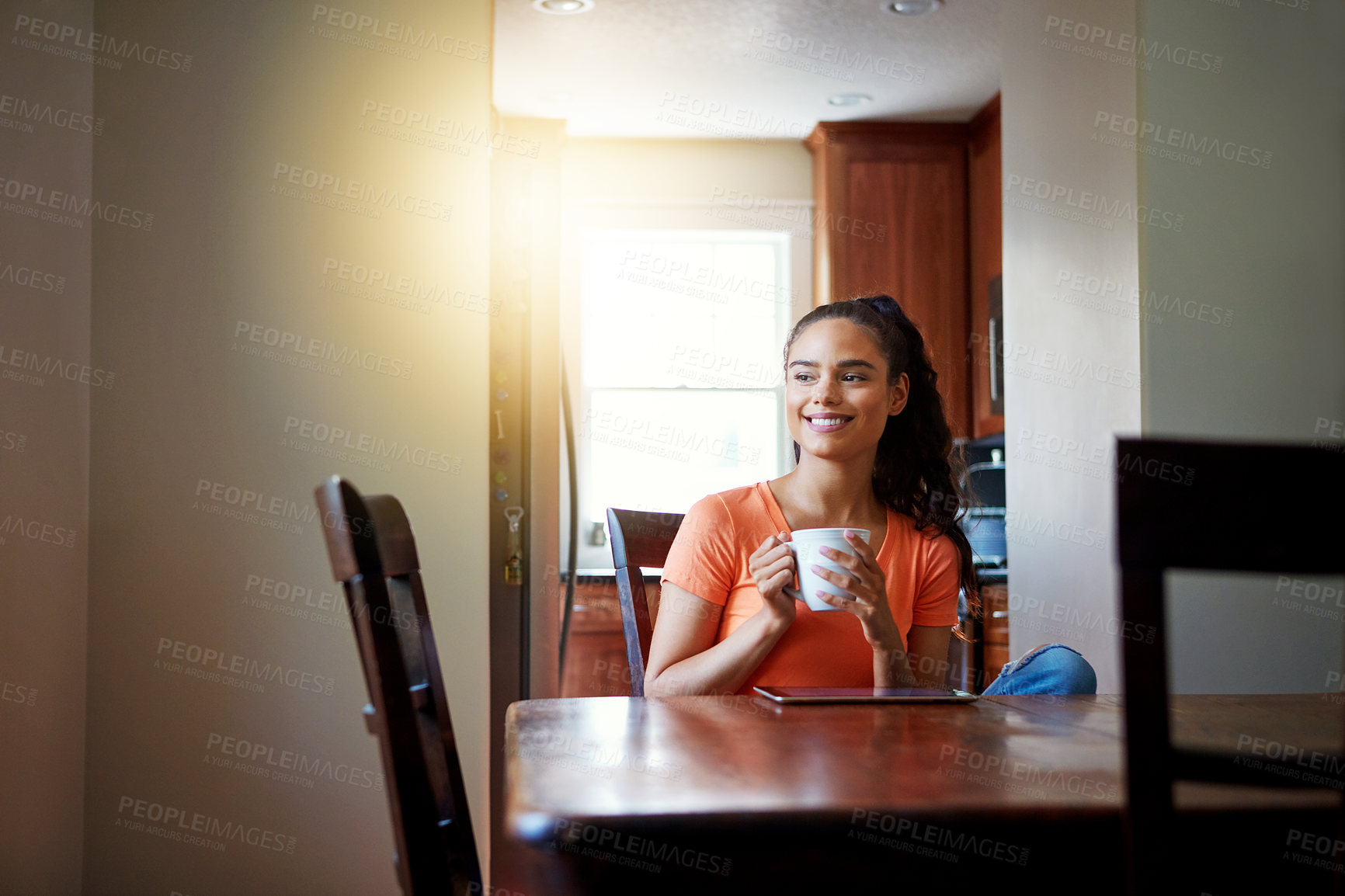 Buy stock photo Shot of a smiling young woman sitting at her dining table at home drinking coffee and using a digital tablet