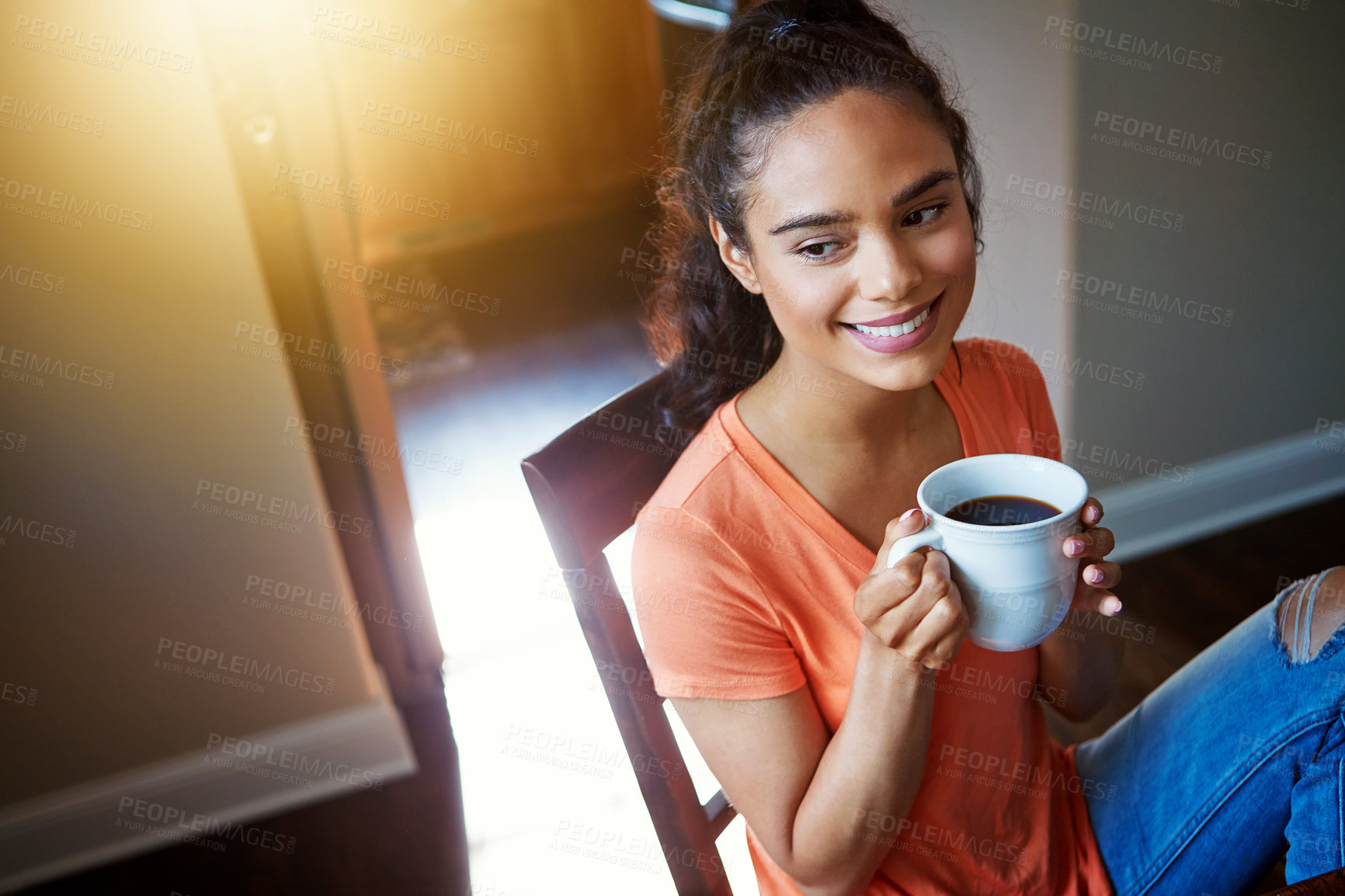 Buy stock photo Shot of a smiling young woman drinking coffee while sitting in a chair at home