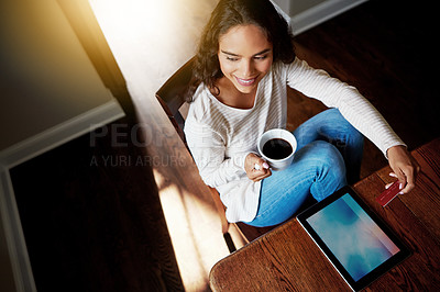Buy stock photo High angle shot of a young woman drinking coffee and shopping online with her digital tablet at home