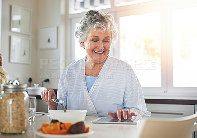 Buy stock photo Cropped shot of a senior woman using a digital tablet while having breakfast at home