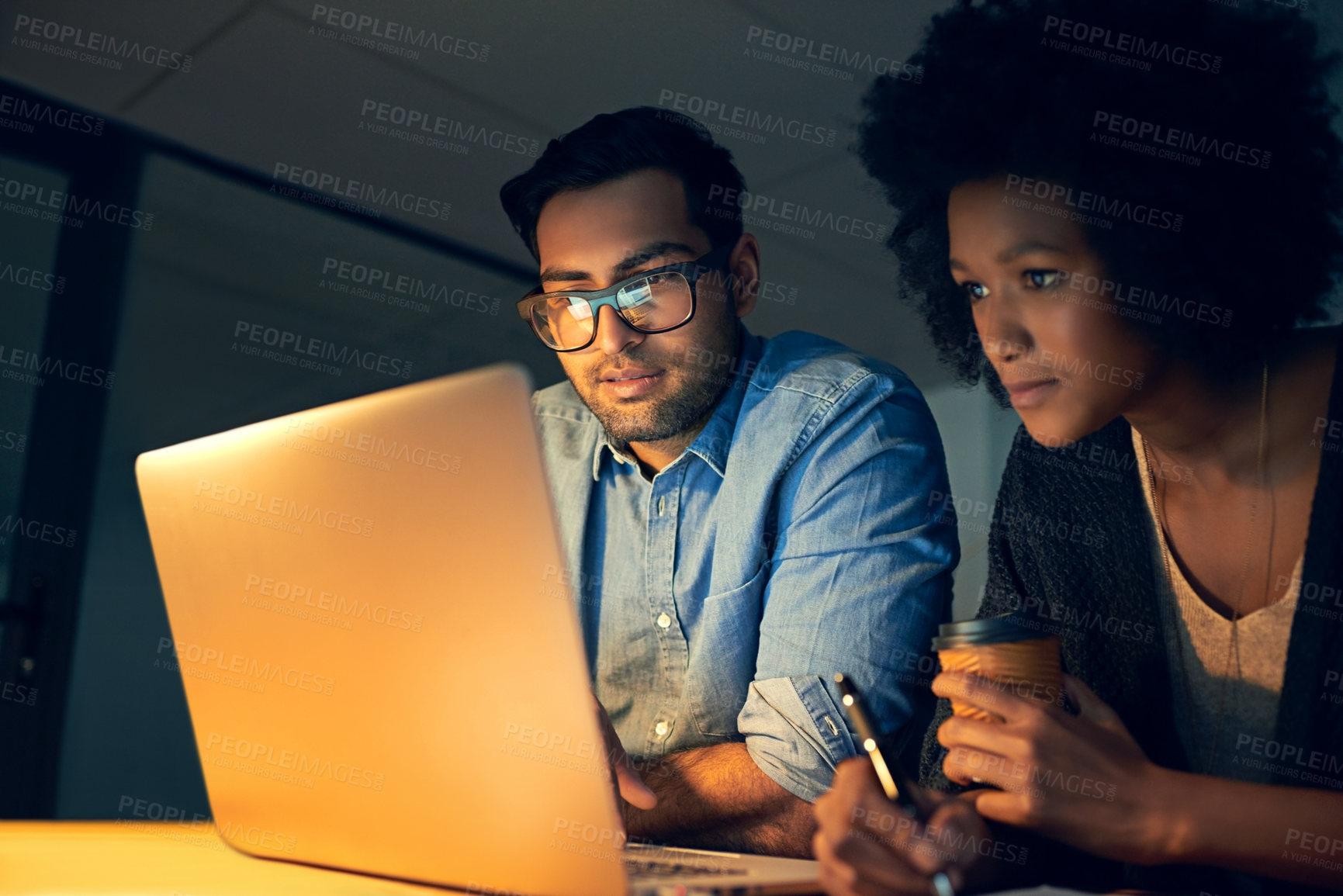 Buy stock photo Cropped shot of two colleagues working late on a laptop in an office