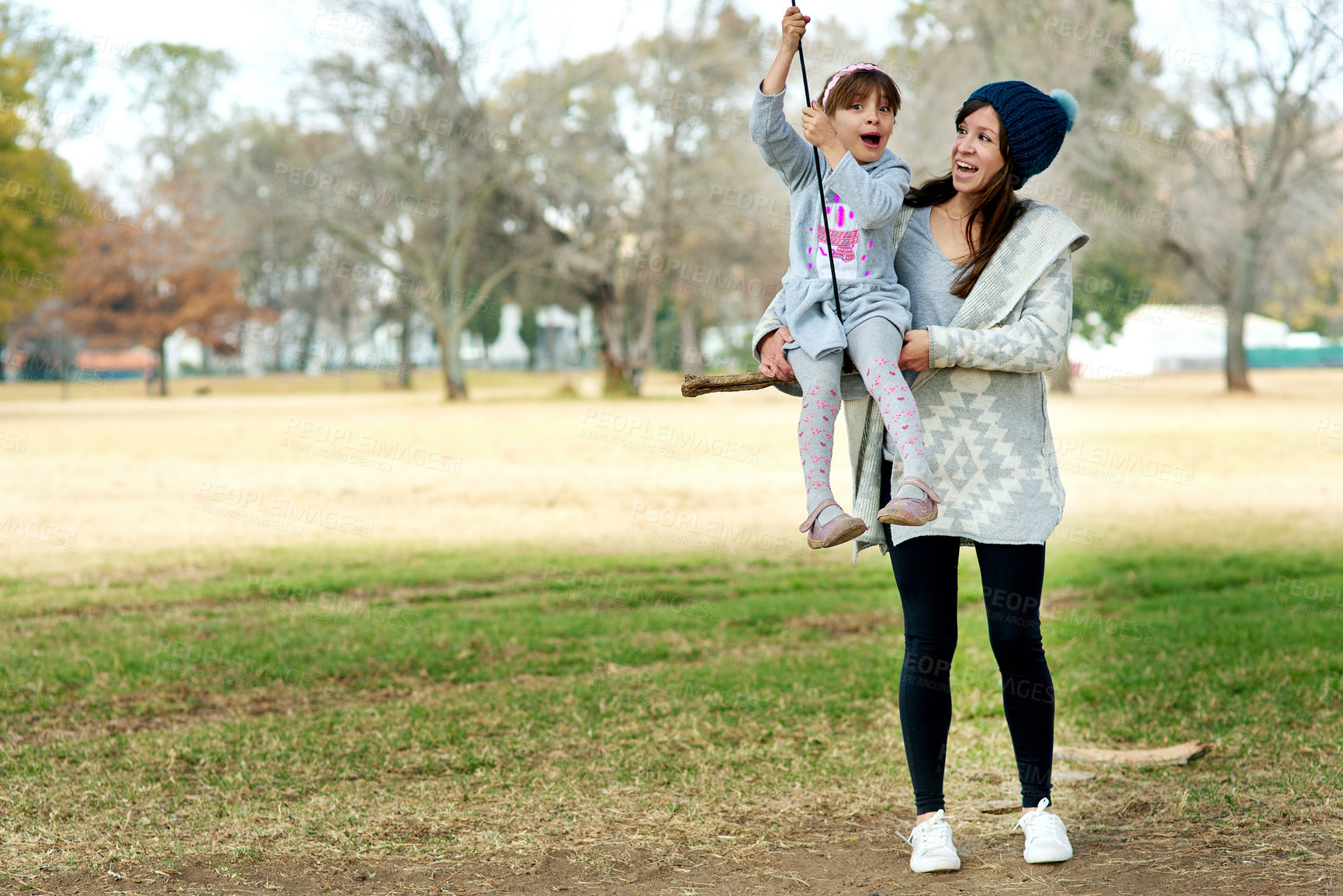 Buy stock photo Shot of a mother pushing her daughter on a swing at the park