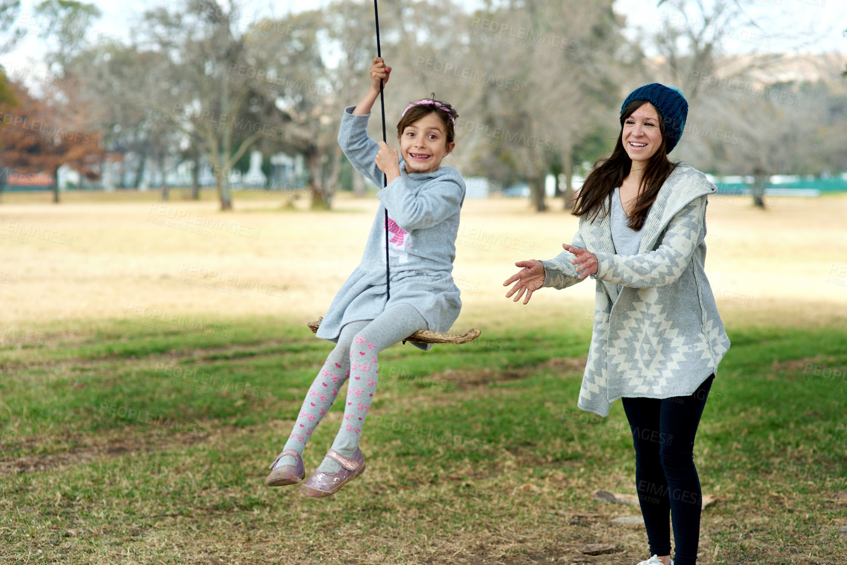 Buy stock photo Shot of a mother pushing her daughter on a swing at the park