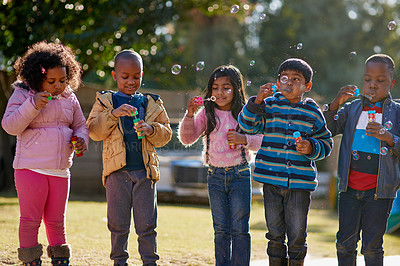 Buy stock photo Cropped shot of a group of little children blowing bubbles together outside