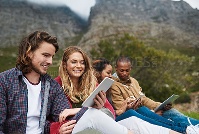 Buy stock photo Shot of a young man showing his tablet to a friend while they hang out outside