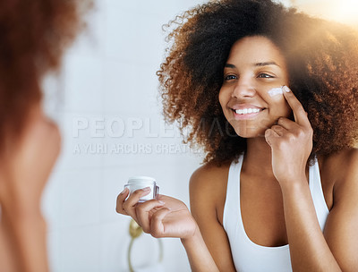 Buy stock photo Shot of an attractive young woman applying moisturizer to her face in front of the mirror