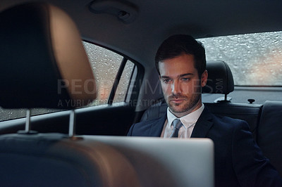 Buy stock photo Shot of a businessman sitting in the backseat of a car working on a laptop