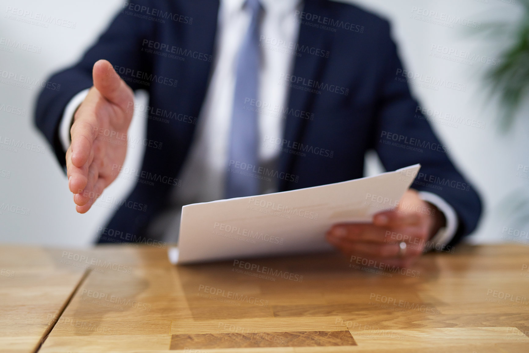 Buy stock photo Cropped shot of a businessman sitting at a desk and holding paperwork extending a handshake