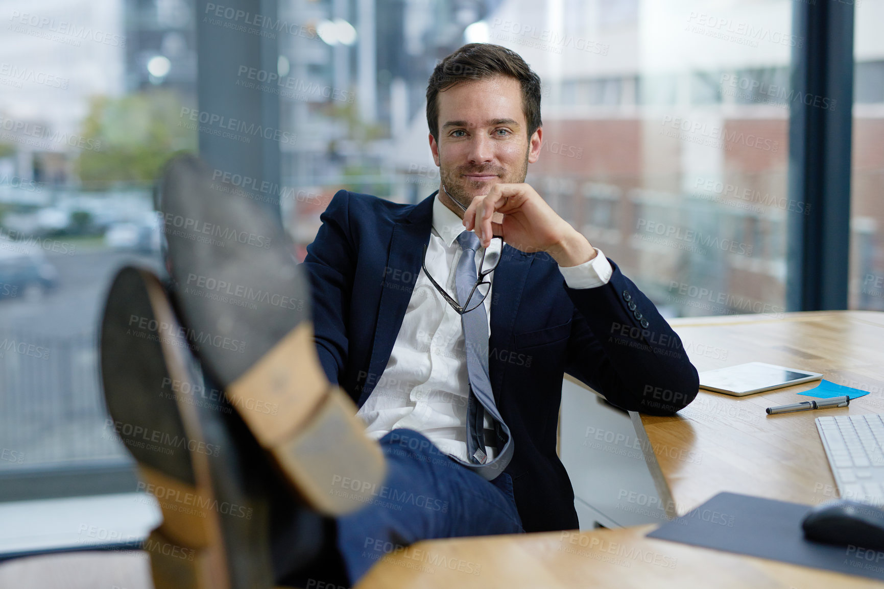 Buy stock photo Portrait of a businessman sitting in an office with his feet resting on his desk