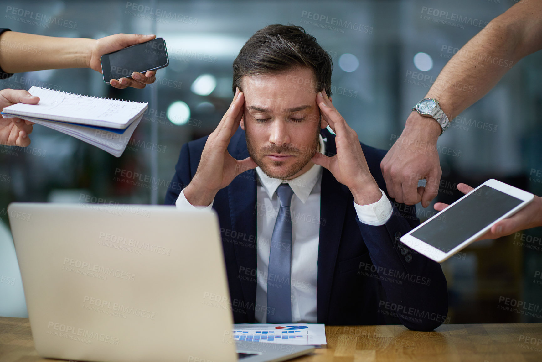 Buy stock photo Shot of a stressed out looking businessman surrounded by demanding colleagues while sitting at a desk in an office