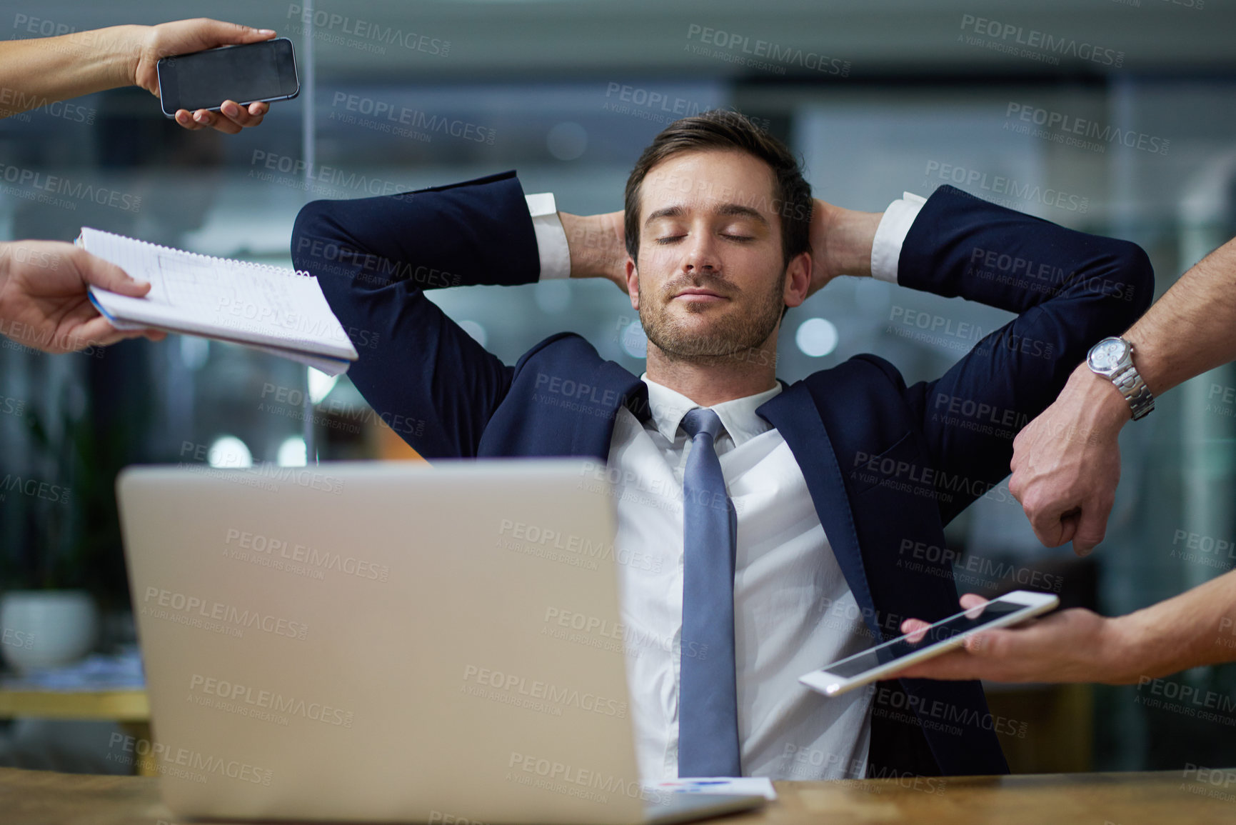 Buy stock photo Shot of a businessman sitting calmly at his desk while surrounded by demanding colleagues in an office