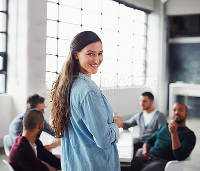 Buy stock photo Portrait of a smiling woman looking over her shoulder while giving a presentation to colleagues in an office