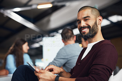 Buy stock photo Portrait of a young man sitting at a table in an office using a digital tablet with colleagues working in the background