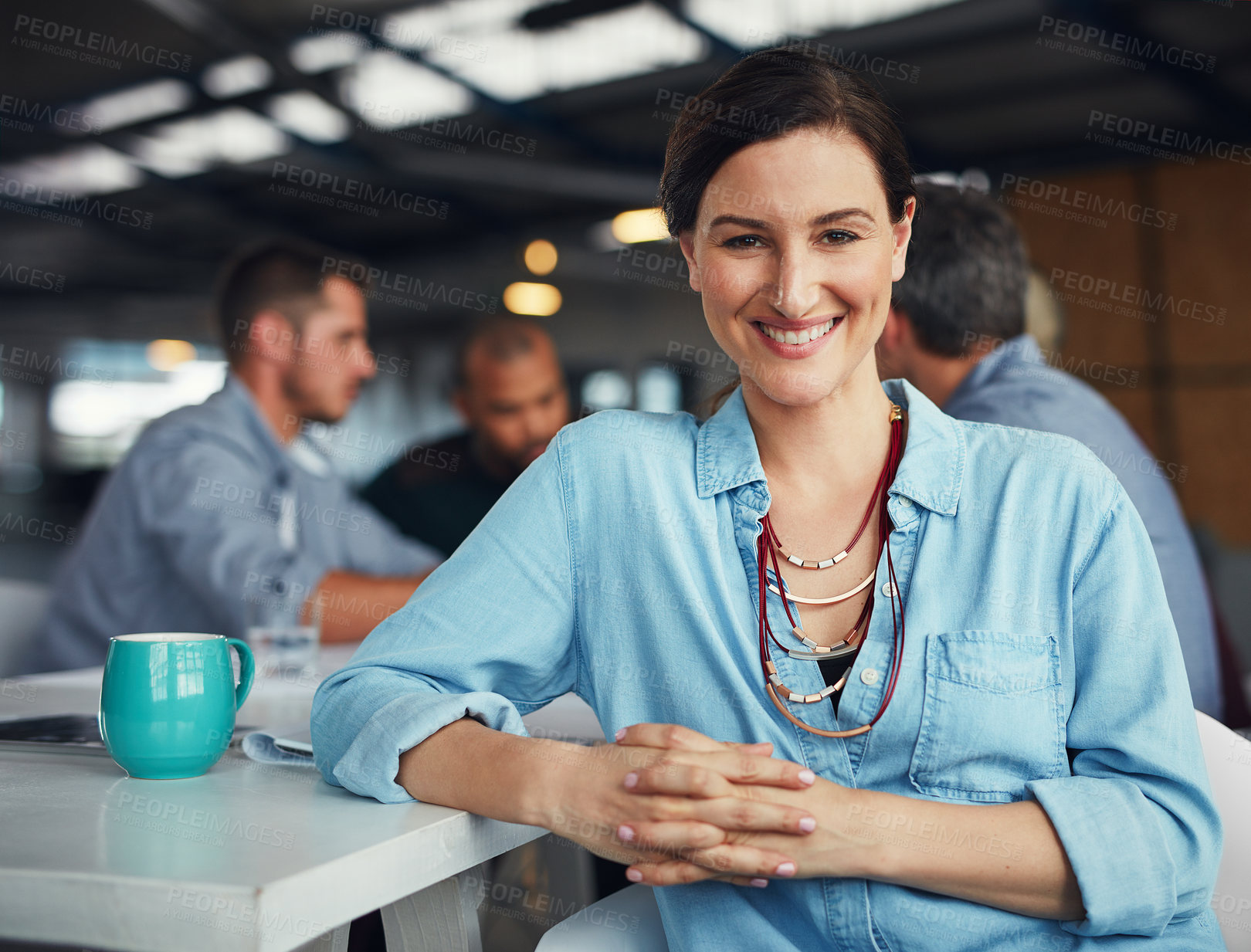 Buy stock photo Portrait of a smiling woman sitting at a table in an office with colleagues working in the background