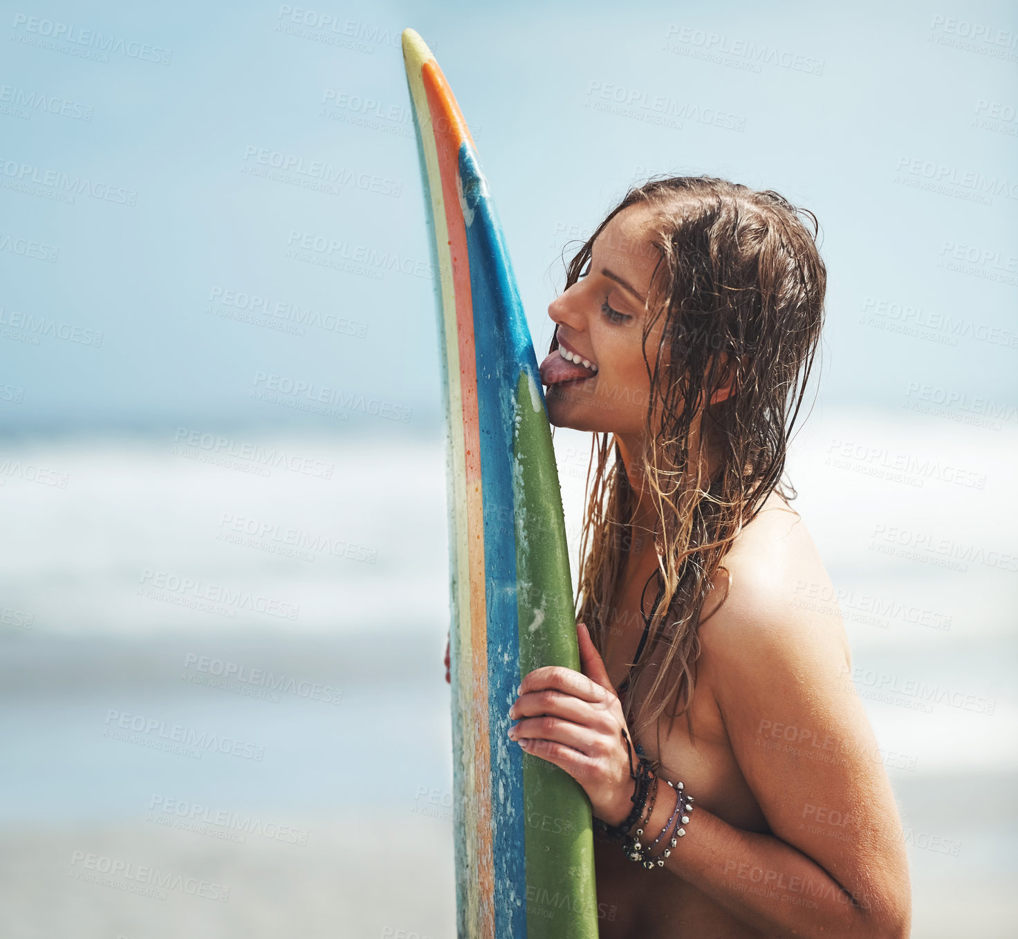 Buy stock photo Shot of an attractive young woman standing on a beach licking her surfboard