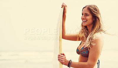 Buy stock photo Shot of an attractive young woman standing on a beach with a surfboard