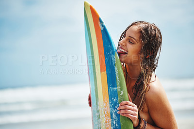 Buy stock photo Shot of an attractive young woman standing on a beach licking her surfboard