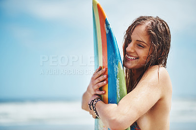Buy stock photo Shot of an attractive young woman standing on a beach hugging her surfboard