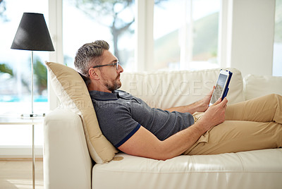 Buy stock photo Man, relax and tablet on living room couch, reading and social media for video, game or movies in home. Mature guy, digital touchscreen and lounge sofa for internet blog, news or web app in house