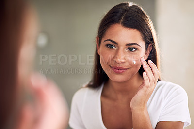 Buy stock photo Shot of a beautiful woman applying moisturizer while looking in the mirror