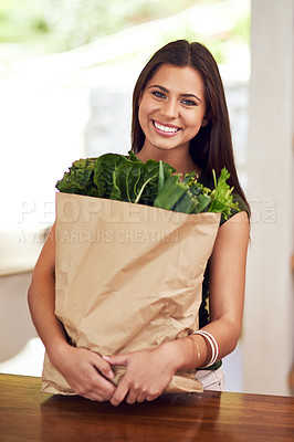 Buy stock photo Portrait of an happy young woman holding a bag of groceries in her kitchen