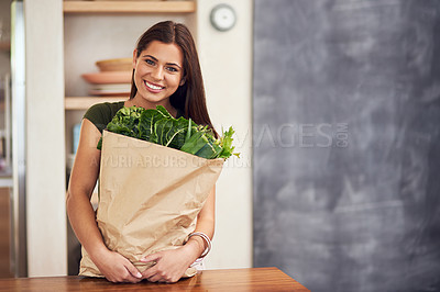 Buy stock photo Portrait of an happy young woman holding a bag of groceries in her kitchen