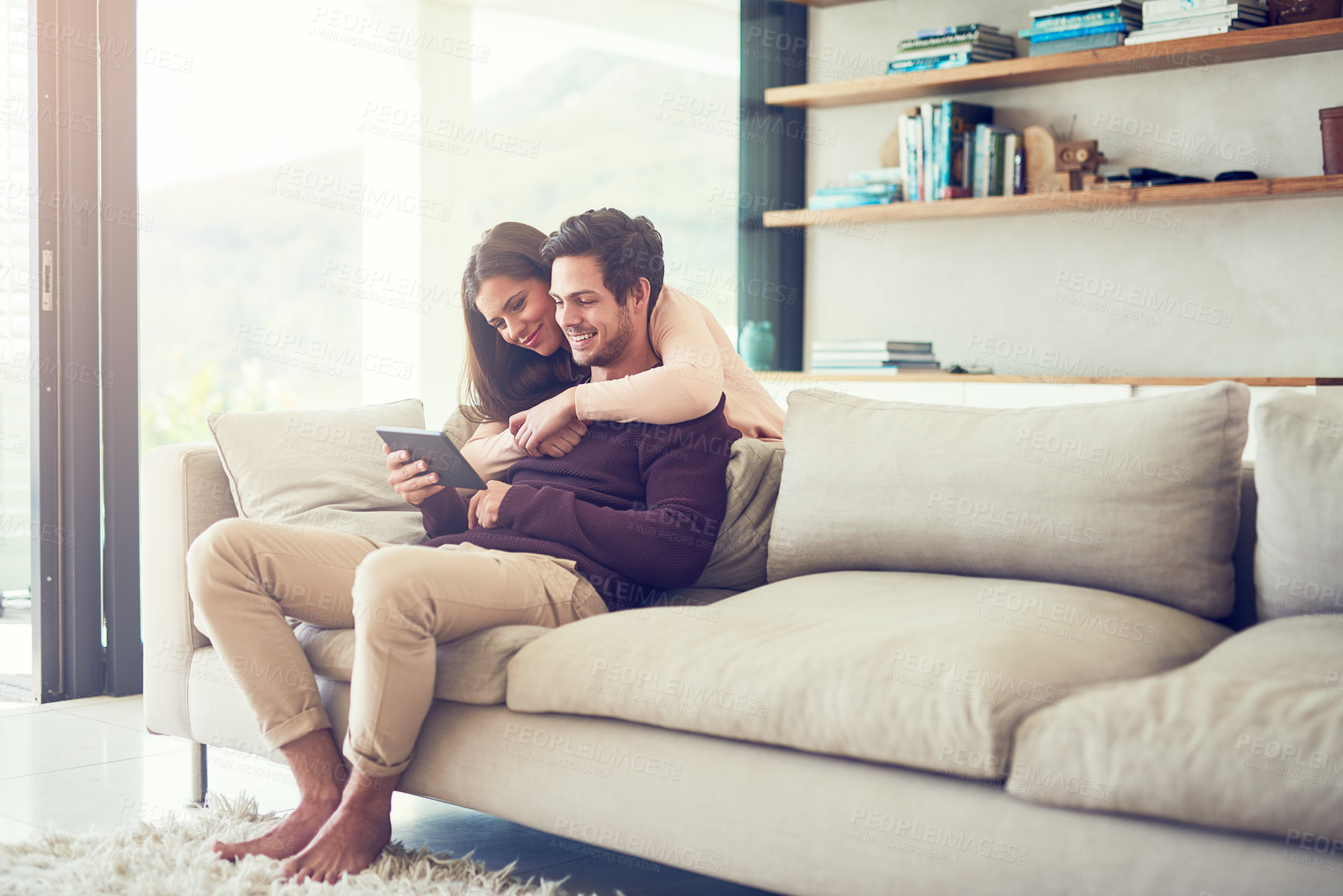 Buy stock photo Shot of a smiling young couple using a digital tablet while relaxing on the sofa at home