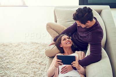 Buy stock photo Shot of a smiling young couple using a digital tablet while relaxing together on the sofa at home