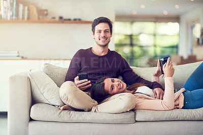 Buy stock photo Portrait of a smiling young couple using digital tablets while relaxing together on the sofa at home