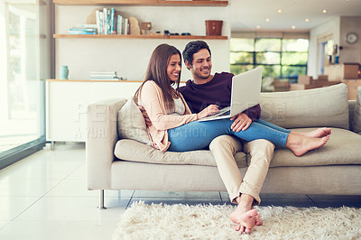 Buy stock photo Shot of a smiling young couple using a laptop while relaxing on the sofa at home
