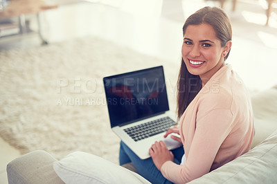 Buy stock photo Portrait of a smiling young woman using a laptop while relaxing on the sofa at home