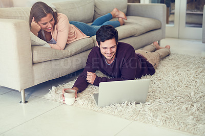Buy stock photo Shot of a smiling young couple using a laptop while relaxing in their living room