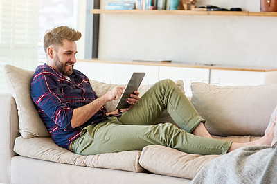 Buy stock photo Shot of a relaxed young man using a digital tablet on the sofa at home