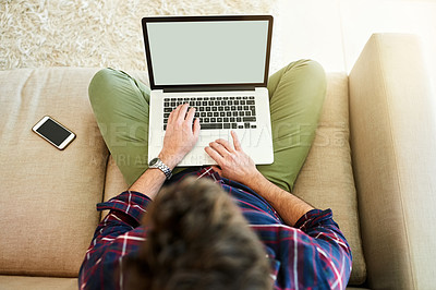 Buy stock photo High angle shot of a young man using a laptop on the sofa at home