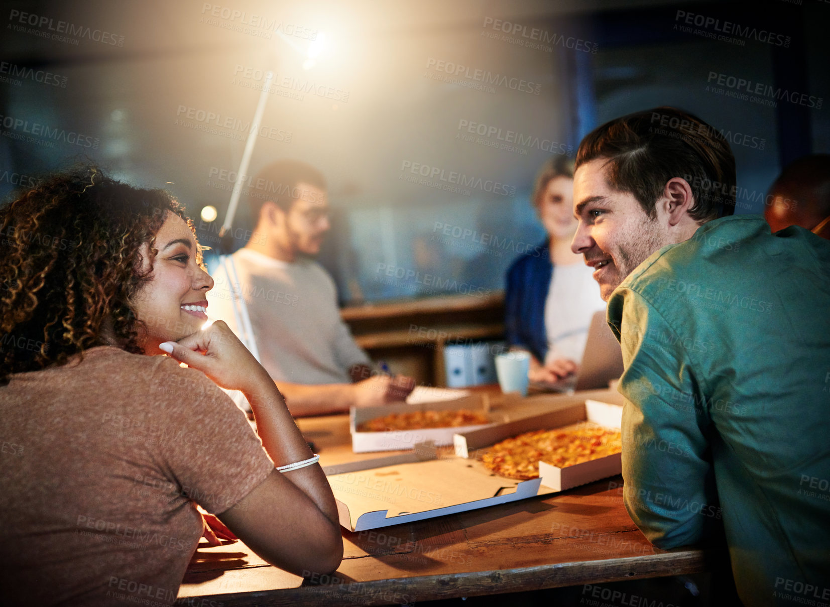 Buy stock photo Shot of a team of young businesspeople eating pizza while working late in the