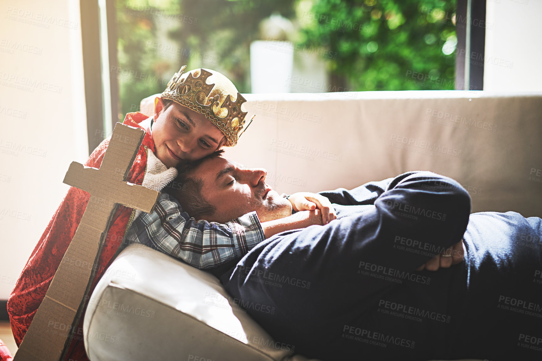 Buy stock photo Shot of a little boy in a king's costume hugging his sleeping father on the couch