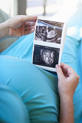 Buy stock photo Shot of an unidentifiable pregnant woman holding a sonogram picture while relaxing at home