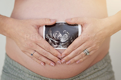 Buy stock photo Shot of an unidentifiable pregnant woman holding a sonogram in front of her belly