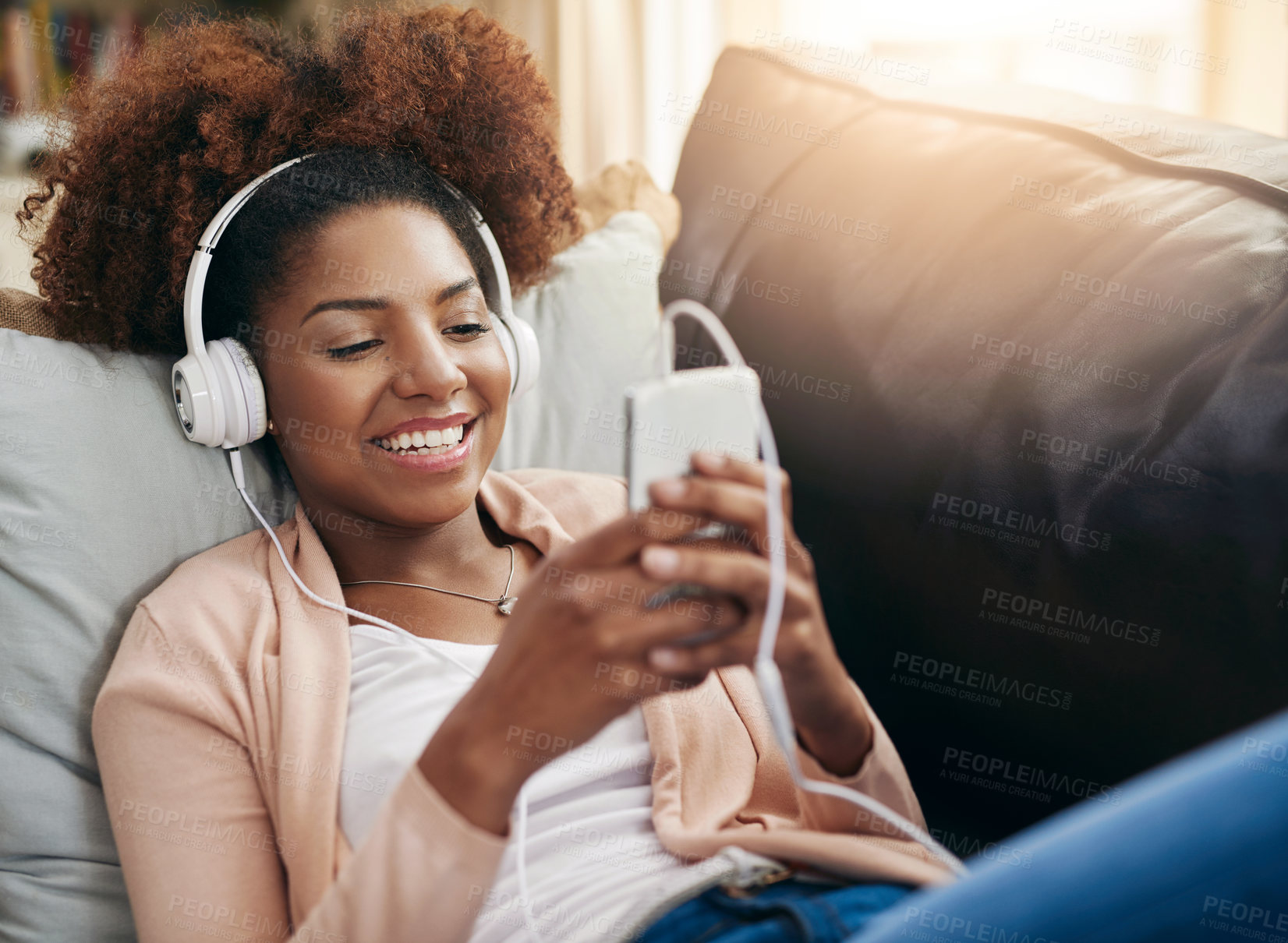 Buy stock photo Relax, phone and happy woman on sofa with headphones, smile and morning streaming in living room. Rest, wellness and girl on couch in home with music, mobile app and smartphone in calm apartment.