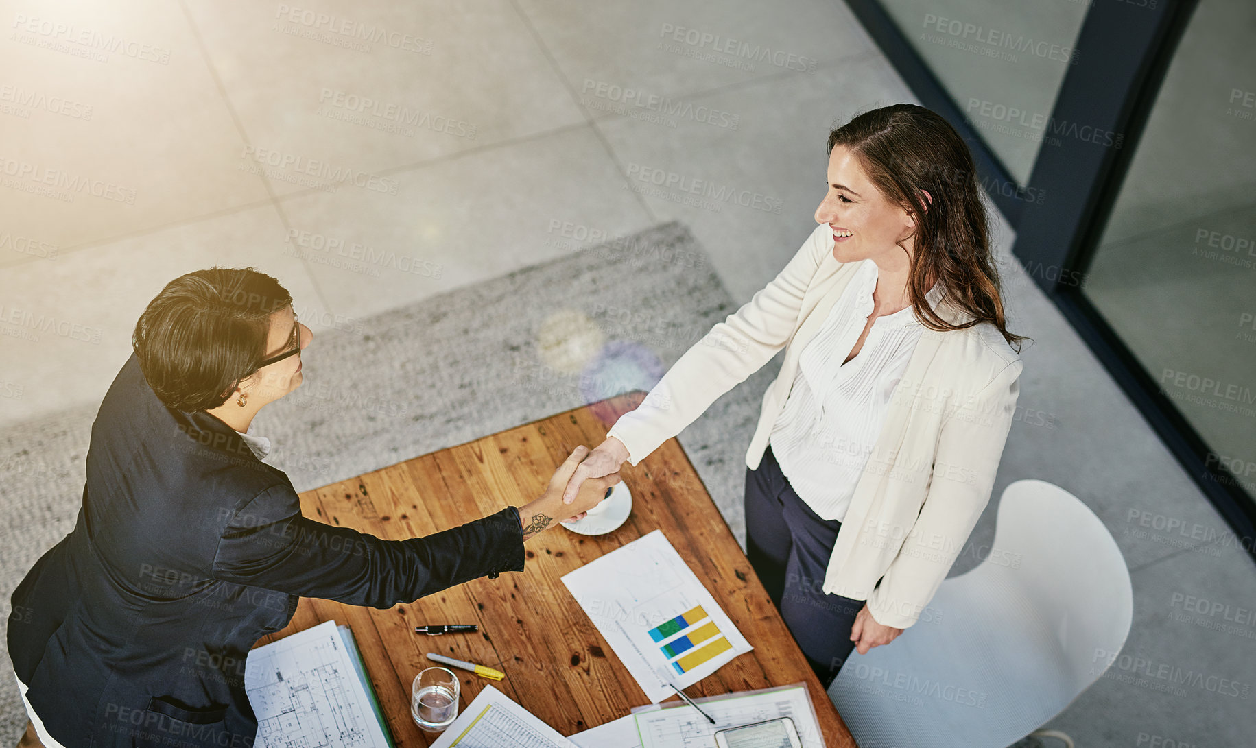 Buy stock photo High angle shot of two businesswomen shaking hands in an office