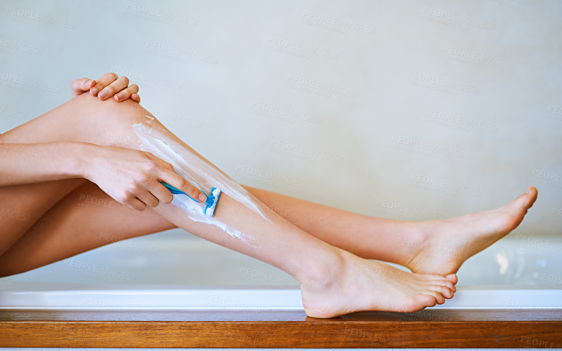 Buy stock photo Cropped shot of a young woman shaving her legs in the bathroom