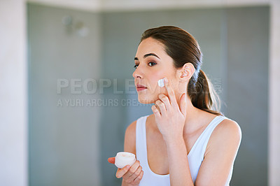 Buy stock photo An attractive young woman applying cream to her face
