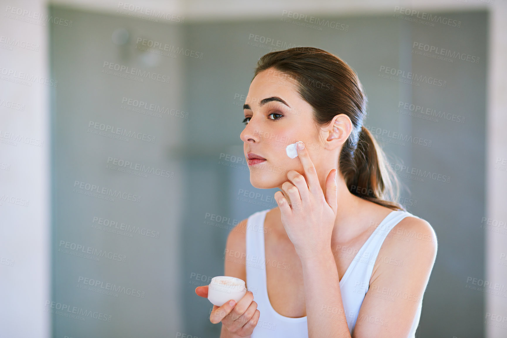 Buy stock photo An attractive young woman applying cream to her face