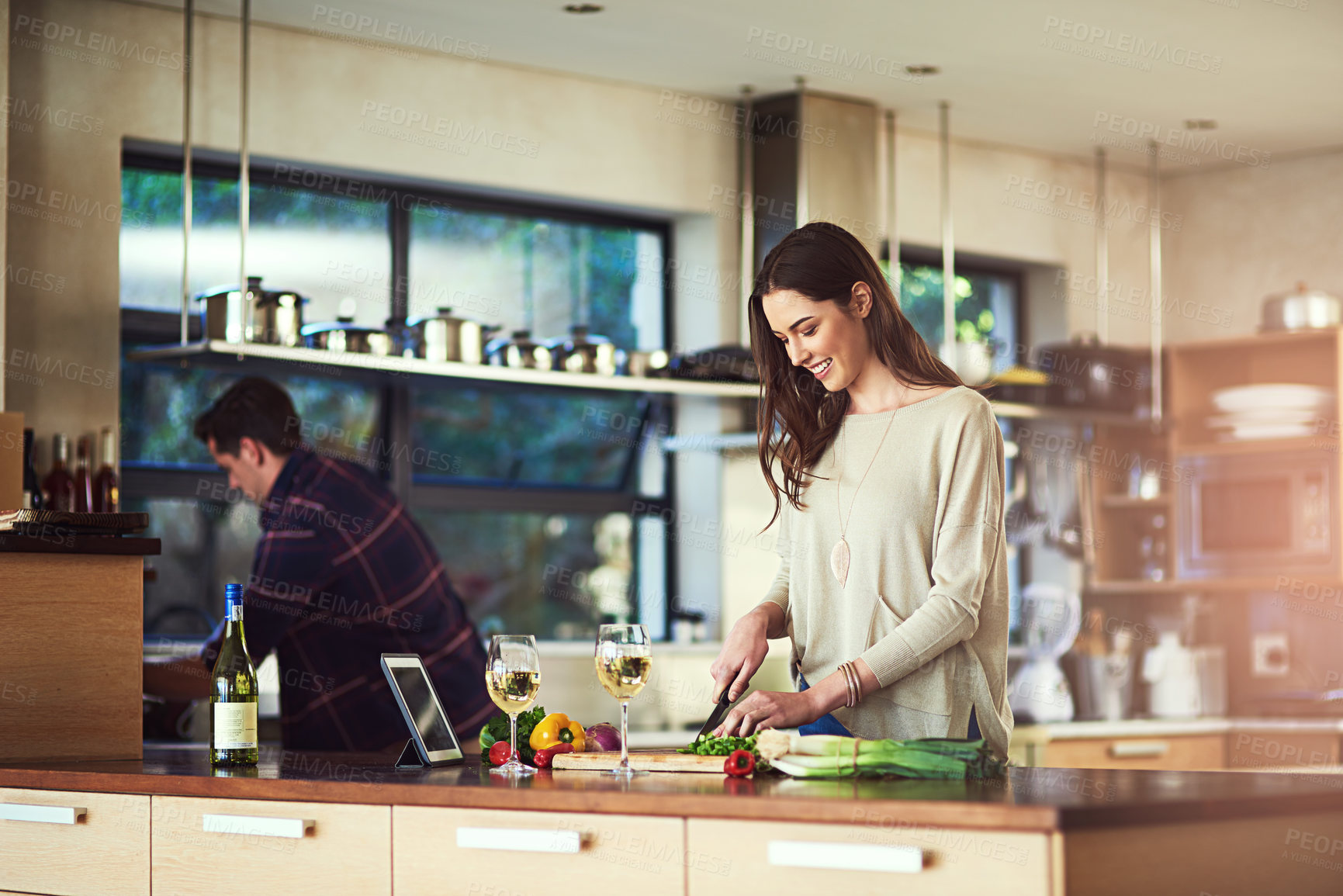 Buy stock photo Cropped shot of a young woman preparing a meal with her boyfriend in the background at home