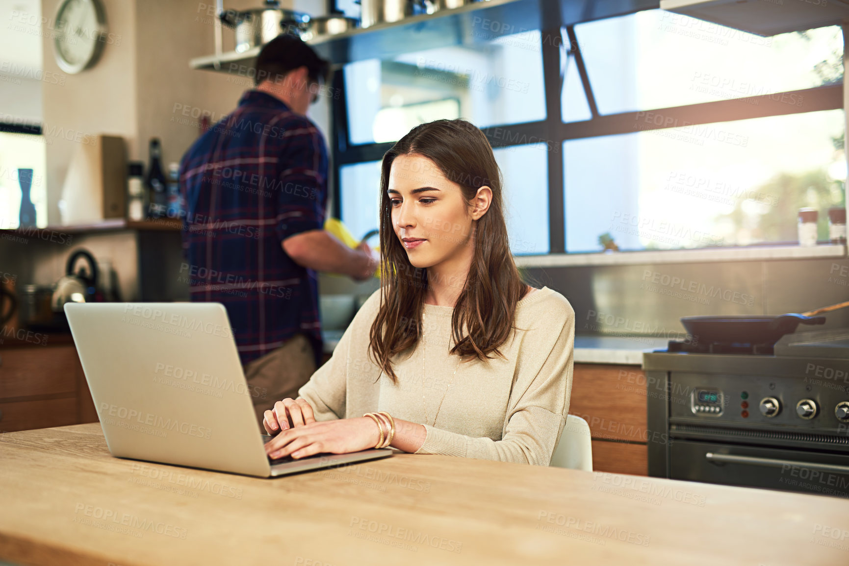 Buy stock photo Cropped shot of a young woman working on a laptop with her boyfriend in the background at home