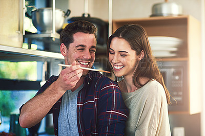 Buy stock photo Cropped shot of a young man giving his girlfriend a taste of the meal he's preparing at home